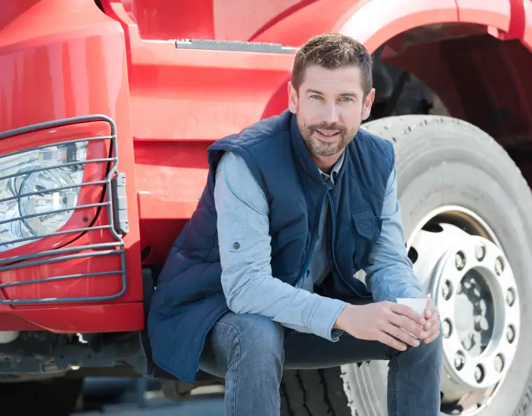 a man sits near a truck with a cup
