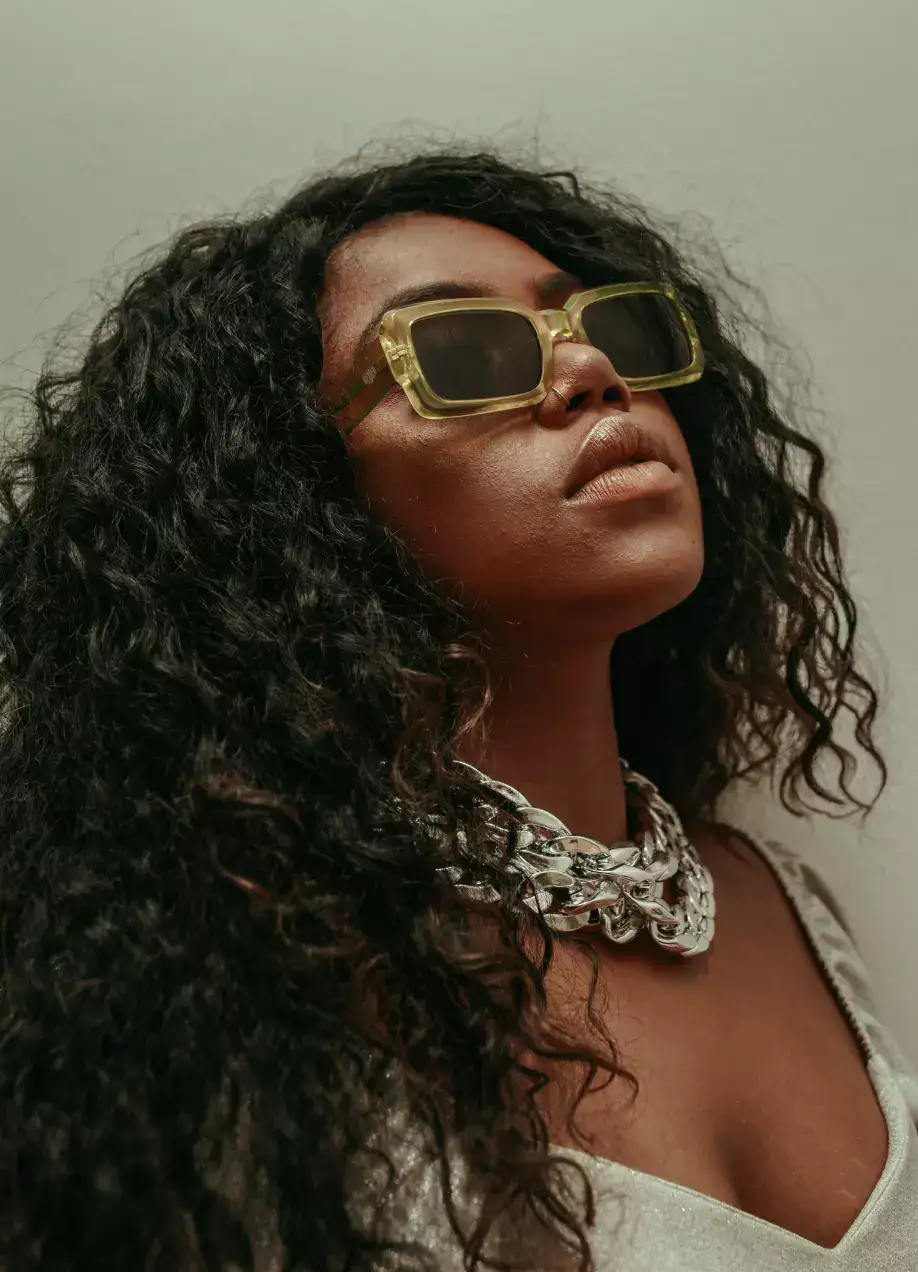 woman with black curly hair and sunglasses wearing a diamond neckles