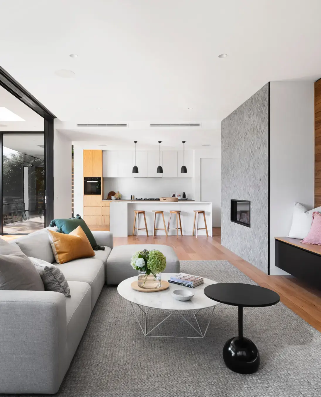 Una moderna sala de estar cuenta con un acogedor sofá seccional gris adornado con cojines coloridos, frente a una elegante mesa de café blanca con un jarrón de flores.