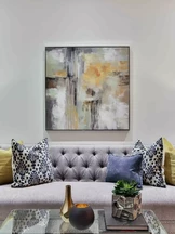 Una elegante sala de estar cuenta con un sofá gris capitoné adornado con almohadas estampadas y lisas en negro, blanco y amarillo.