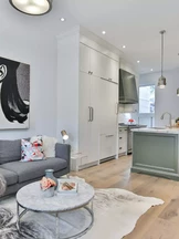 Una moderna sala de estar y área de cocina cuenta con un sofá gris con almohadas de colores, una mesa de café redonda de mármol y una alfombra de piel de vaca.