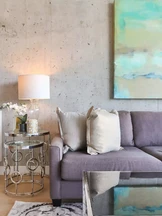 Una moderna sala de estar cuenta con un sofá gris con lujosos cojines, una elegante mesa auxiliar de vidrio con una lámpara decorativa.