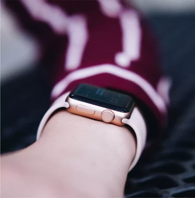 A close-up of a person wearing a rose gold smartwatch with a light pink band, set against a background featuring a maroon and white patterned sleeve.