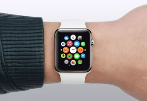 A person wearing a smartwatch with a white band, displaying a colorful array of app icons on the screen, is shown on a wrist with a dark green sleeve.