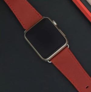 A smartwatch with a sleek, rectangular face and a vibrant red band rests on a dark surface, showcasing its modern design.