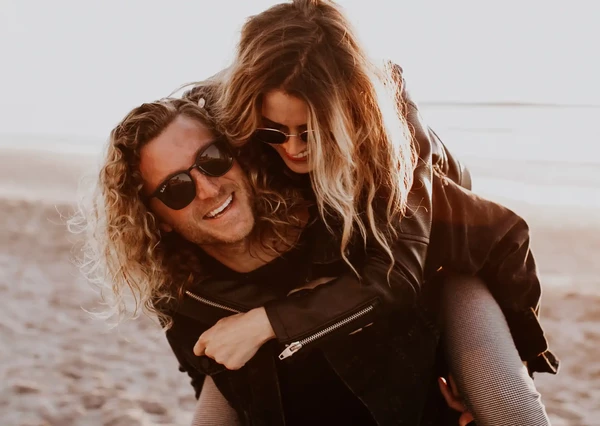 A joyful couple is enjoying a playful moment on the beach, with the woman giving the man a piggyback ride.