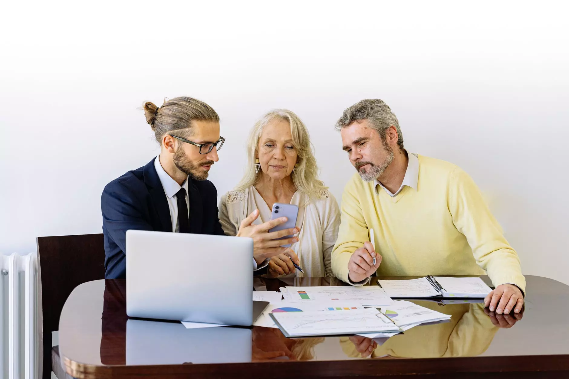 two men and a woman are sitting at a table and looking at the phone