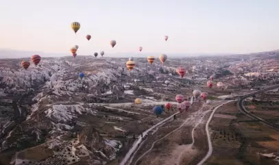 صورة لعدد كبير من البالونات المحلقة في خلفية تلال مغطاة بالرمال.