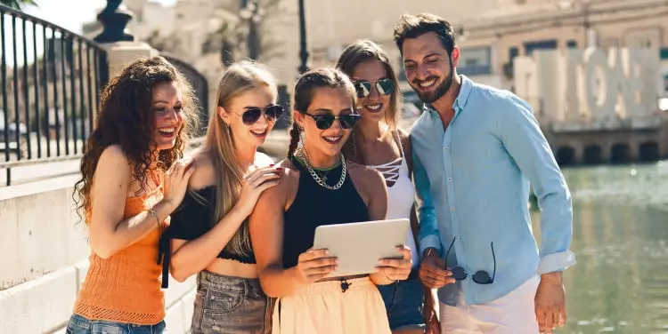 صورة لخمسة أشخاص، أربع فتيات ورجل واحد، يشاهدون شيئًا ما على جهاز لوحي تحمله الفتاة التي في المنتصف.