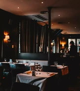 Slabě osvětlená restaurace se pyšní úhledně prostřenými stoly s bílými ubrusy, sklenicemi na víno a ubrousky.