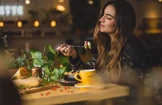 Žena s dlouhými vlasy si užívá jídlo v útulné restauraci a v ruce drží vidličku s kouskem jídla.