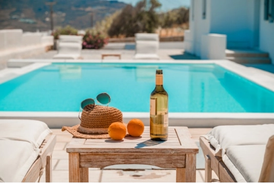 oranges, wine and sunglasses beside the teal pool