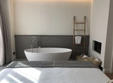 A modern bedroom features a freestanding white bathtub against a gray accent wall, with a wooden ladder holding a towel beside it.
