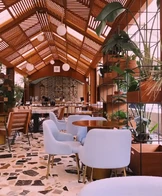 A stylish café interior featuring light blue chairs around round wooden tables, set on a terrazzo floor.