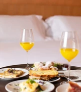 A cozy breakfast setup on a round table features two glasses of orange juice and an assortment of dishes
