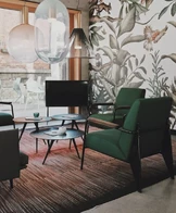 A stylish living room features two green armchairs and a black TV on a stand, set against a wall with a floral mural.