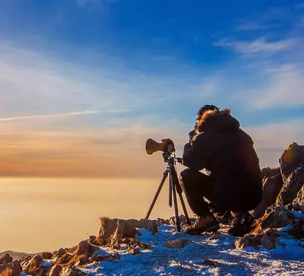 Ein Mann sitzt mit einer Kamera auf einem Berg.