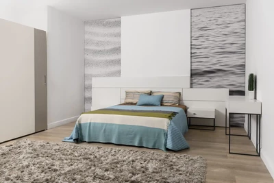 Moderní ložnice má postel s modrobéžovou pruhovanou dekou, odpovídající polštář a texturovaný koberec na dřevěné podlaze.