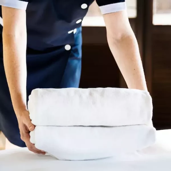 Osoba skládající bílé ručníky na posteli