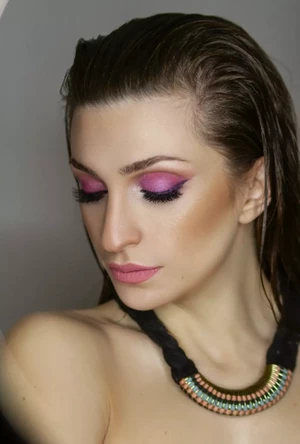 Žena s mokrými vlasy hledí dolů a ukazuje zářivý růžový oční make-up a jemné konturování.