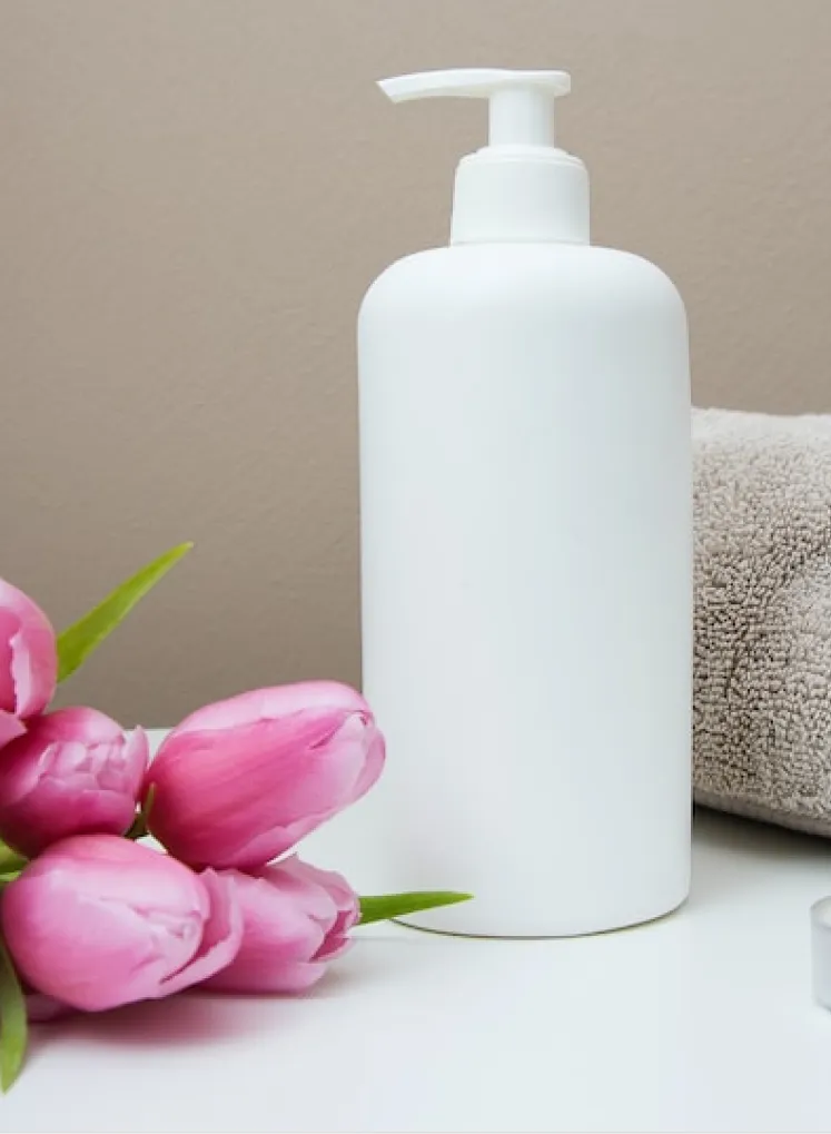 a white jar of soap stands on the sink next to a pink flower