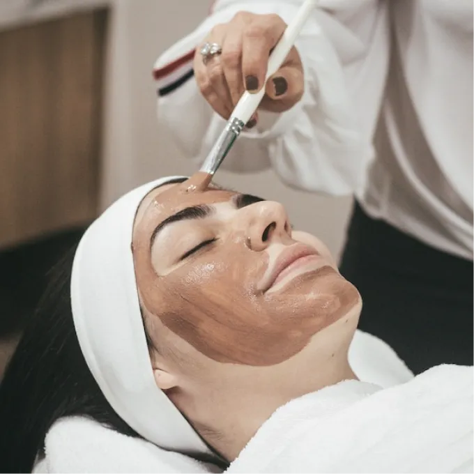 a girl with her eyes closed near a master who is applying a mask to her face