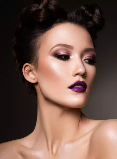 Mergina su aukšta šukuosena ir violetinėmis lūpomis žiūri į šoną