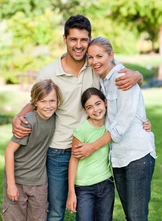 Eine glückliche vierköpfige Familie steht eng beieinander in einem üppig grünen Park und lächelt warmherzig.