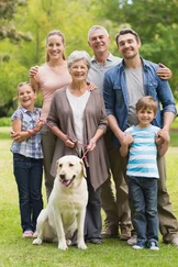 Eine lächelnde sechsköpfige Familie, bestehend aus einer älteren Frau, zwei Erwachsenen, zwei Kindern und einem Labradorhund