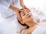 Eine Frau liegt mit geschlossenen Augen auf einer Massageliege und genießt eine entspannende Gesichtsmassage.