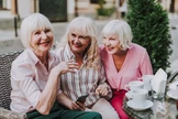 Drei ältere Damen mit weißem Haar sitzen zusammen in einem Straßencafé, lächeln und genießen die Gesellschaft der anderen.