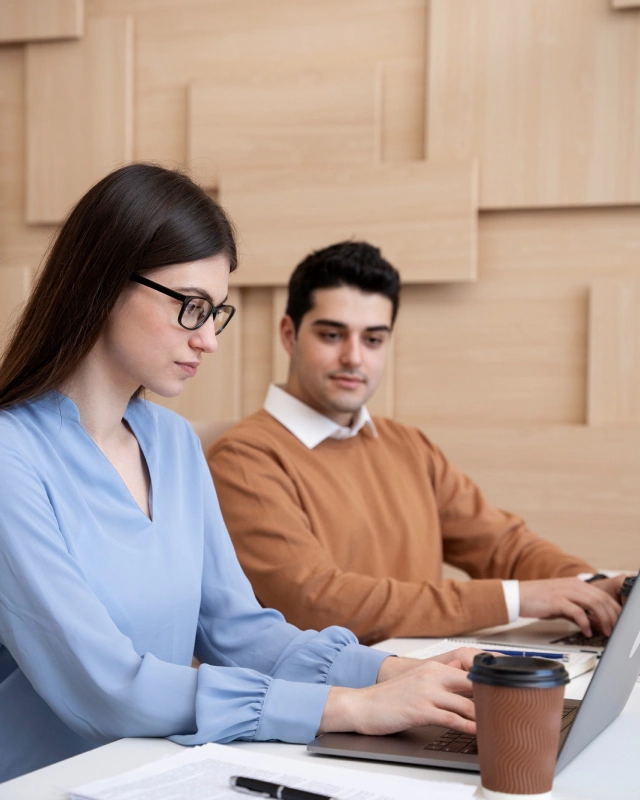 Zwei Personen arbeiten an einem Tisch mit Kaffeetassen an ihren Laptops.