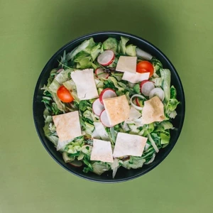 A fresh salad with mixed greens, cherry tomatoes, cubes of chicken, and croutons served in a black bowl