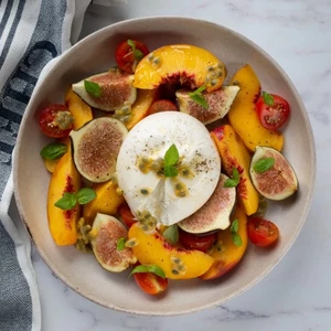 A vibrant salad with sliced peaches, figs, and fresh strawberries, topped with creamy burrata cheese on a white plat