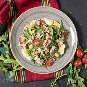 A fresh salad with arugula, cherry tomatoes, and sliced chicken on a plate atop a colorful striped napkin