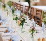 Ein wunderschön gedeckter Esstisch mit Blumenarrangements in Glasvasen, umgeben von ordentlich angeordneten Weingläsern und Servietten mit blau-kariertem Muster