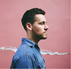 a young guy in a denim shirt stands sideways to the camera