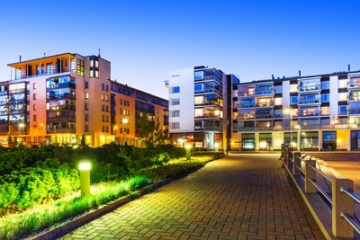 Vakarinis miesto vaizdas su moderniais pastatais ir apšviestais takais