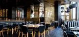 Nowoczesne wnętrze restauracji z ciemnymi drewnianymi podłogami, czarnymi krzesłami i złotymi akcentami