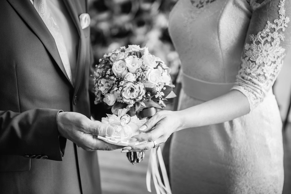sposi che tengono gli anelli e il bouquet
