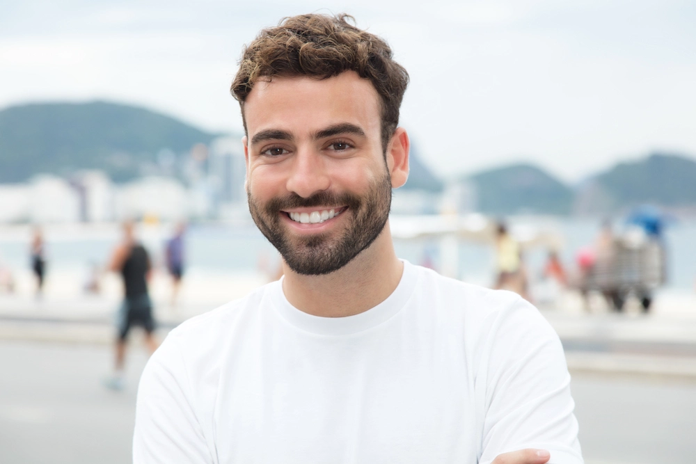 Un ragazzo giovane con i capelli biondi e la barba sorride ampiamente