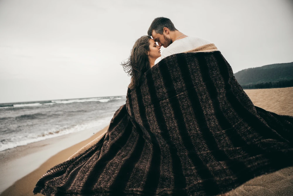 un ragazzo e una ragazza si abbracciarono e si nascosero in una coperta sulla spiaggia