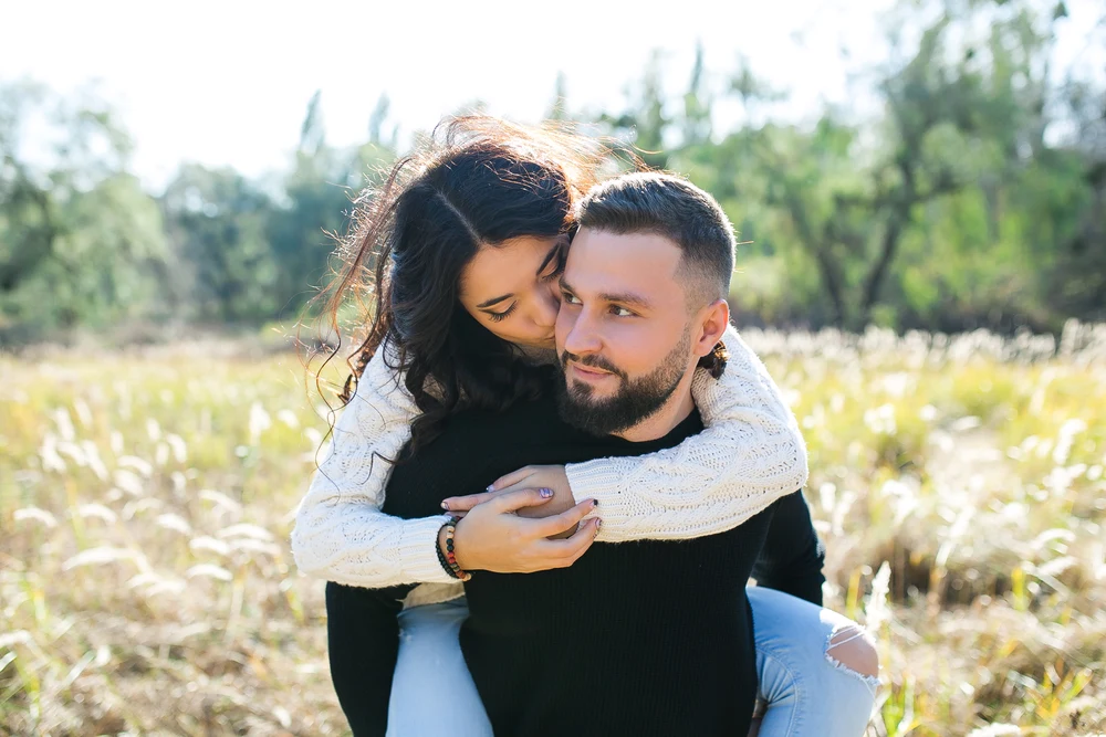 il ragazzo tiene la ragazza sulla schiena ed entrambi sorridono ampiamente