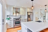 A modern kitchen featuring white cabinetry, a stainless steel stove with a hood, and a matching refrigerator