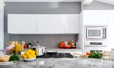 A modern kitchen features sleek white cabinets, a marble countertop, and a silver stovetop with a pot