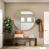 A stylish entryway features a large round mirror with a wooden frame above a wooden bench adorned with decorative pillows