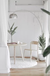 A minimalist room features a round wooden table with a matching chair on a fluffy white rug