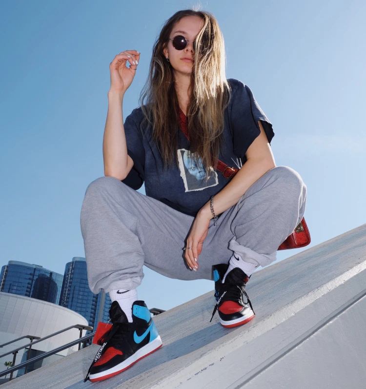 Dívka ve sportovním oblečení a tmavých kulatých brýlích dřepí