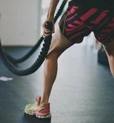 Eine Person trainiert mit Battle Ropes in einem Fitnessstudio. Sie trägt bunte Turnschuhe und Shorts mit auffälligen Mustern, was eine konzentrierte und dynamische Trainingsszene zeigt.
