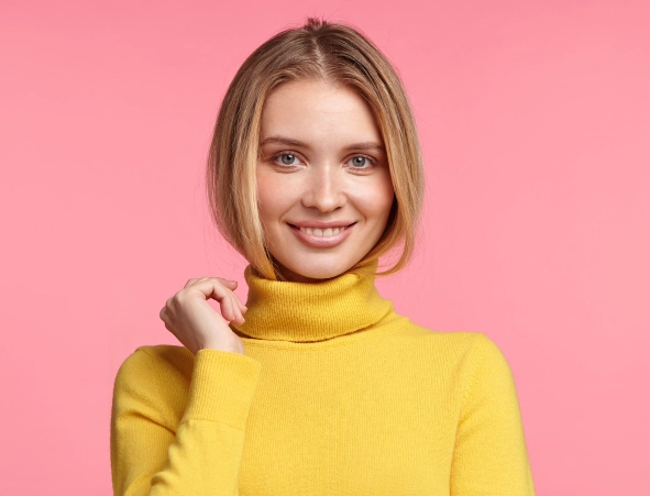 Una joven rubia con un suéter amarillo sonríe dulcemente.